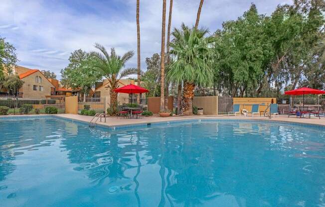 A swimming pool surrounded by palm trees and red umbrellas.