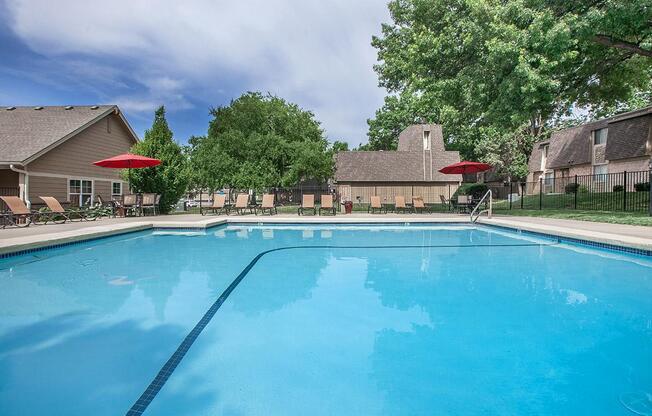 A clean outdoor swimming pool with trees and lounge seating.