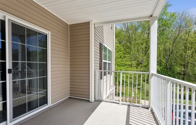 A screened porch with a white railing and a view of trees.