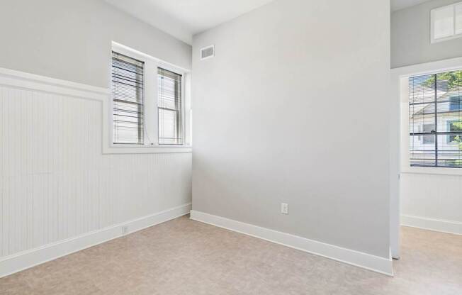 an empty bedroom with two windows and white walls