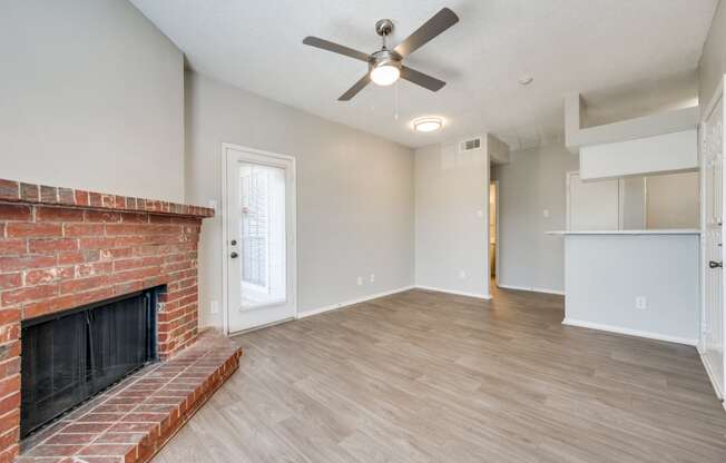 an empty living room with a brick fireplace and a ceiling fan