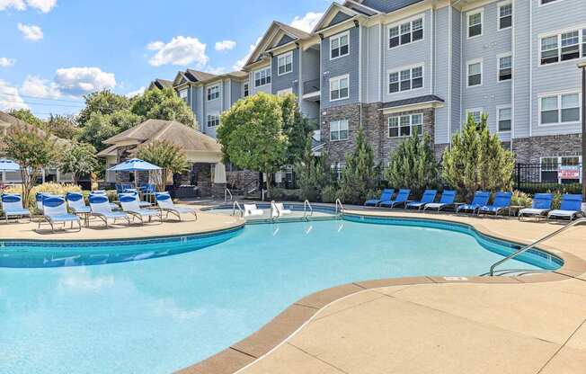 A swimming pool surrounded by blue lounge chairs and apartment buildings.
