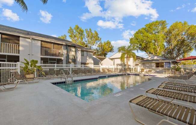 A swimming pool surrounded by sun loungers and apartment buildings.