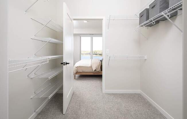 A white walk-in closet with shelves and a doorway leading to a living room.