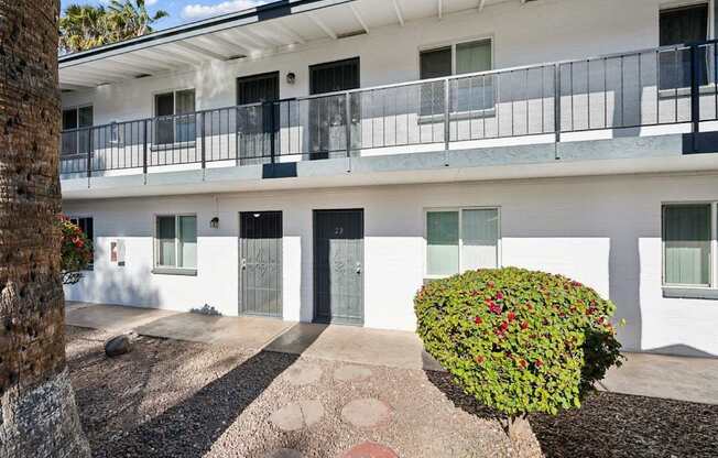 A white building with a balcony and a green bush in front.