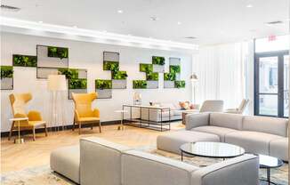 A living room with a grey couch, yellow chairs and a glass table.