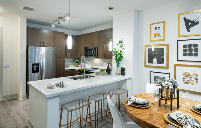Open-concept kitchen and dining space with a 4-person dining table, ash-gray wood-style floors, dark modern cabinets, stainless steel appliances, and white quartz countertops.