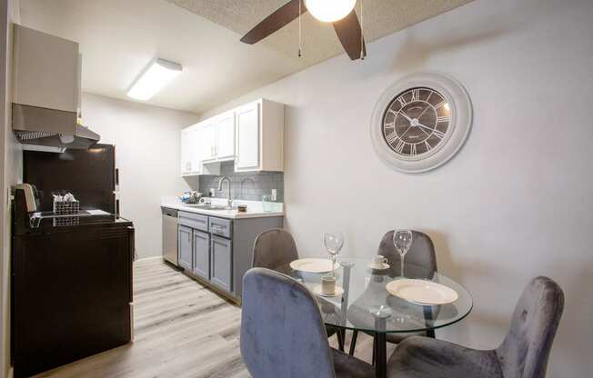 a dining room table with chairs and a kitchen with a clock on the wall