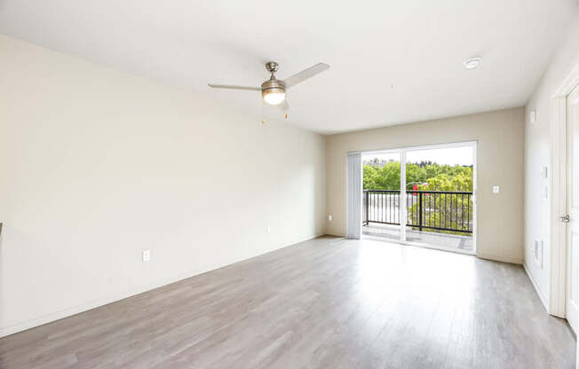 A spacious room with a ceiling fan and sliding glass doors leading to a balcony.