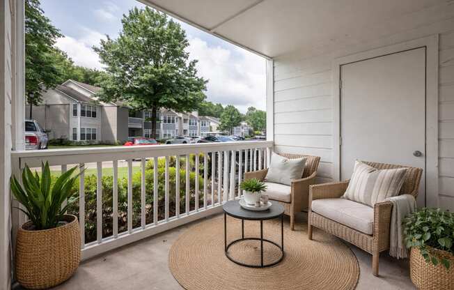 A patio with a white railing, a wicker chair, and a table with a plant on it.