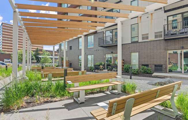 A wooden bench with a green armrest is in the foreground of a modern outdoor seating area.