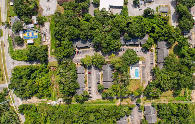 A bird's eye view of a residential area with houses, trees, and a swimming pool.