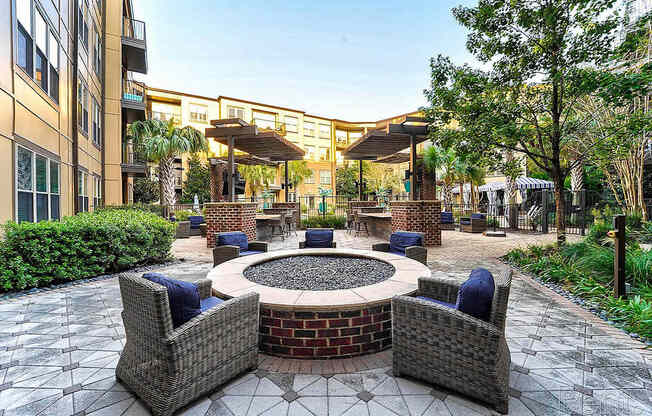 A patio with a fire pit surrounded by chairs and a building in the background.