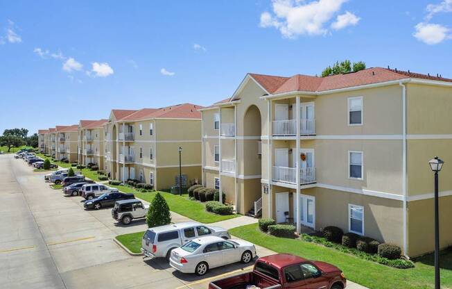 A row of apartment buildings with cars parked in front.