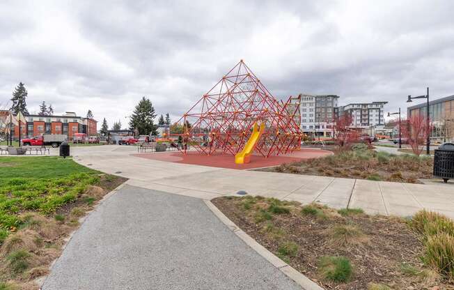 A playground with a red and yellow structure in the middle of a concrete area.
