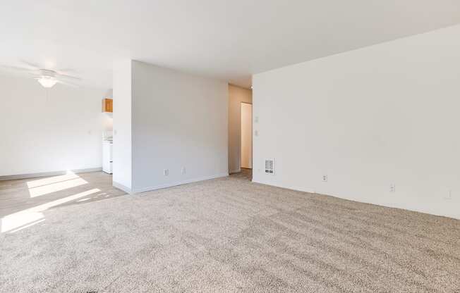 the living room and dining room of an apartment with white walls and carpet