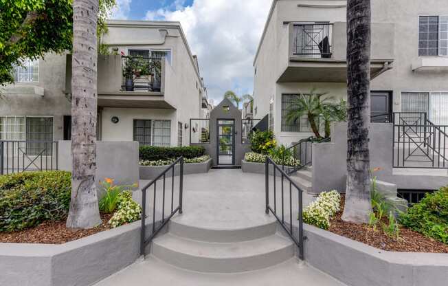 Apartment complex entry from the street with 2 stairs leading up to the community entry door. Palm trees are on both sides of the stairs. 