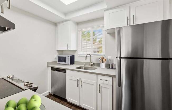 A kitchen with a refrigerator, sink, and green apples on the counter.