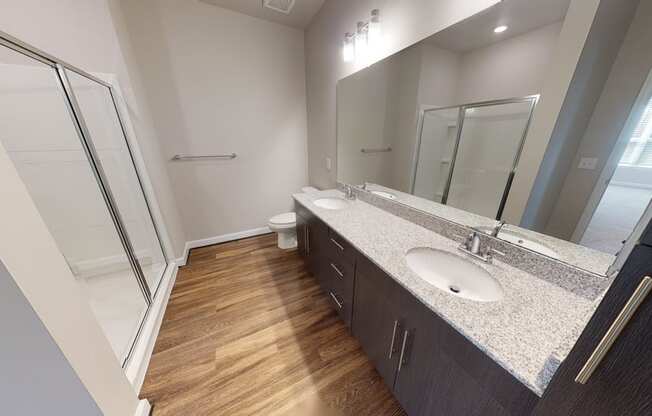 Bathroom with dual sinks, dark cabinets, toilet and walk-in shower