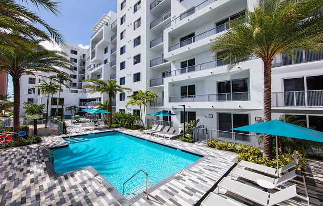 a swimming pool in front of a building with palm trees at Saba Pompano Beach, Pompano Beach, 33062