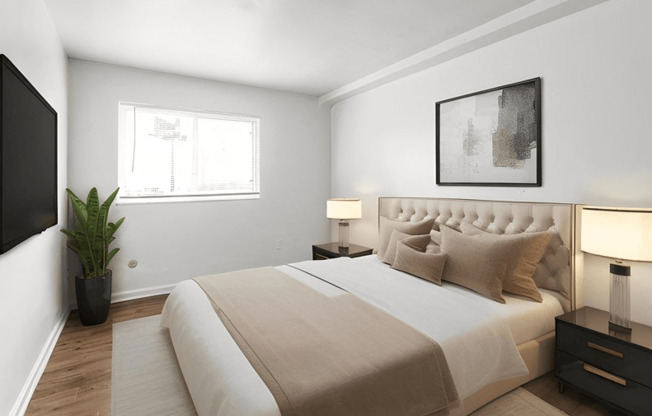 A bedroom with a large bed, a plant, and a painting on the wall.