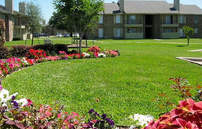 a lush green lawn with flowers in front of an apartment building at Wymberly Pointe, Grand Prairie, TX, 75052