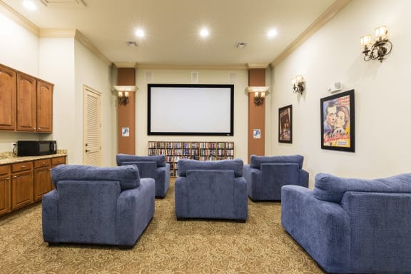 Rapallo Apartments community theater room with a screen mounted on the wall, individual sofa chairs and a movie library