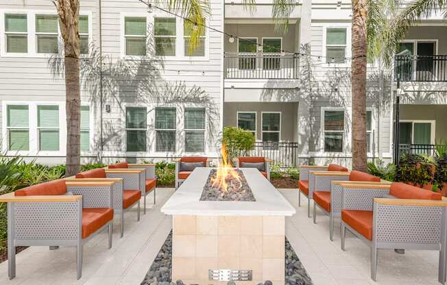 A fire pit is surrounded by chairs in front of a building.