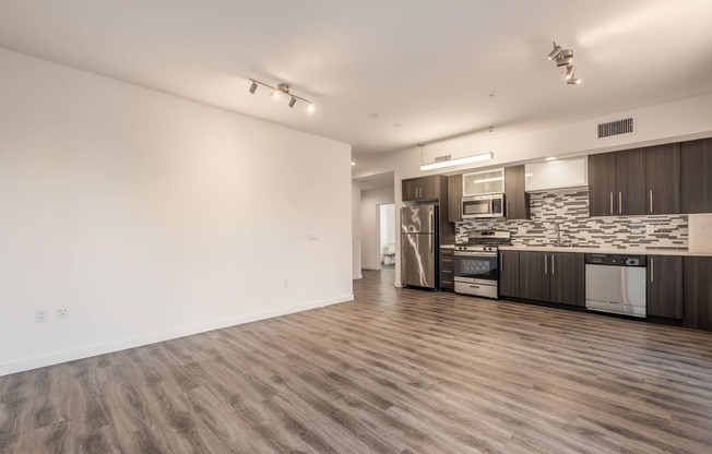 an empty living room and kitchen with wood flooring and a stainless steel refrigerator