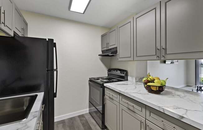 Kitchen with Grey Cabintery, Plank Flooring, and Efficient Appliances, Providing View into Spacious Living Area at Campo Basso Apartment Homes, Lynnwood, 98087