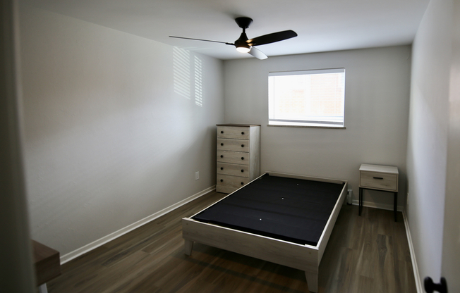Inviting bedroom with modern ceiling fan, hardwood floors, and ample natural light, perfect for relaxation.