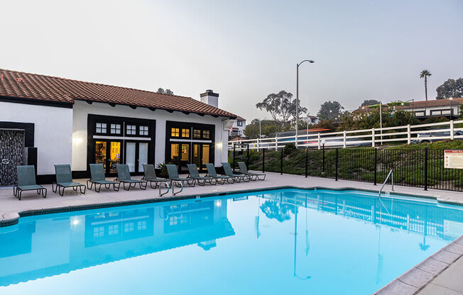 A swimming pool in front of a house with a black fence.