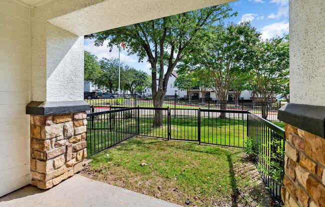 Covered patio with stone columns and fenced grassy yard at Villas of Vista Ridge.