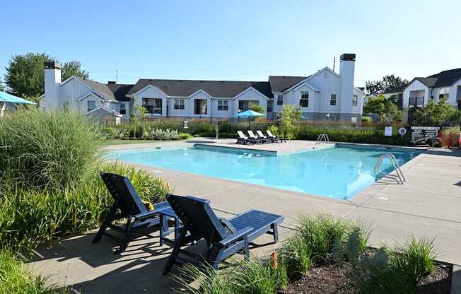 A pool surrounded by chairs and a grassy area.