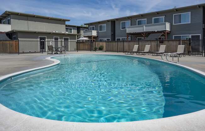 a swimming pool with chairs around it in front of an apartment building