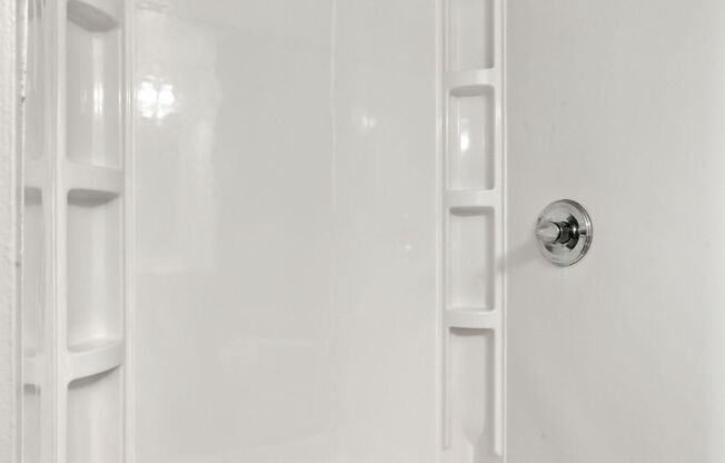 A white bathroom with a shower stall and a drain in the tub.