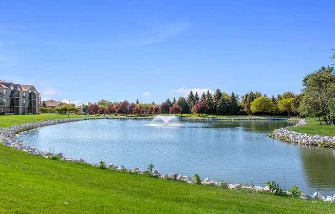 A serene pond surrounded by a well-manicured lawn and a stone wall at Oak Shores Apartments in Oak Creek, WI