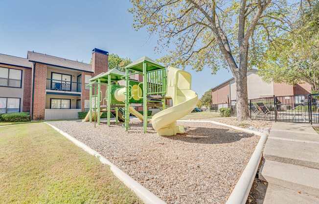 A playground with a green and yellow slide in front of a building.