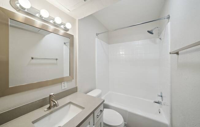 a bright bathroom with a sink toilet and shower and a mirror Woodlands of Plano in Plano, TX