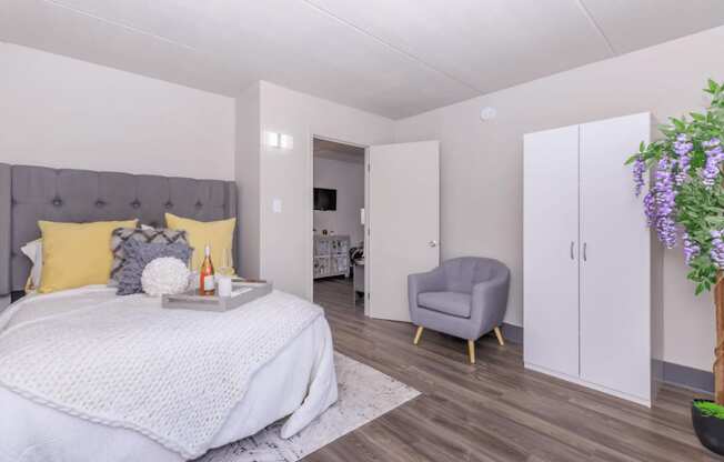 A bedroom with a bed, chair, and a plant.