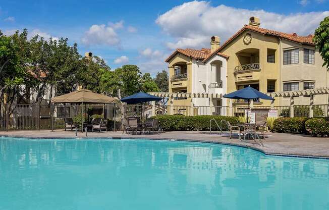 A large swimming pool in front of a building with a blue umbrella.