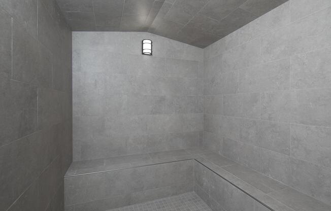 A modern, minimalist shower space featuring gray tiled walls and floor, along with a simple light fixture. The design emphasizes clean lines and a spacious, open feel with a bench built into the wall.