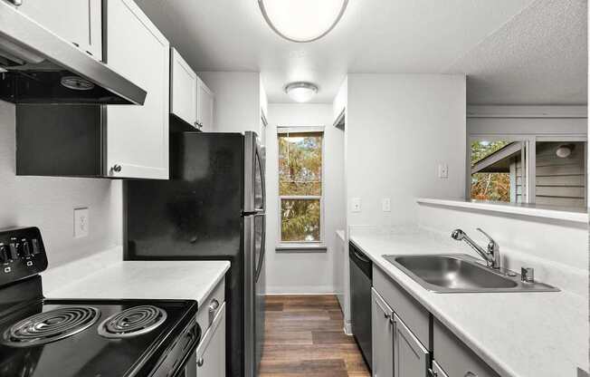 A black stove top oven sits in a kitchen with white cabinets and a black fridge.