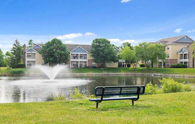 Serene lakefront view at Center Point Apartments with fountain, bench seating, and tree-lined apartment buildings in the background.