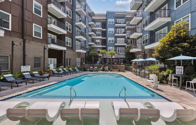 an outdoor swimming pool with lounge chairs and umbrellas in front of an apartment building