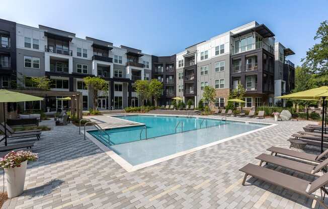 a swimming pool with lounge chairs and umbrellas in front of an apartment building at Century University City, Charlotte, 28213