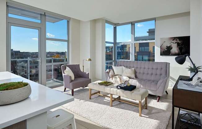 A modern living room with a grey sofa, a white table, and a large window with a view of the city.