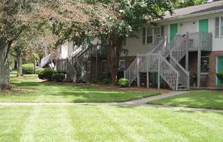 the front of a building with stairs and grass and trees