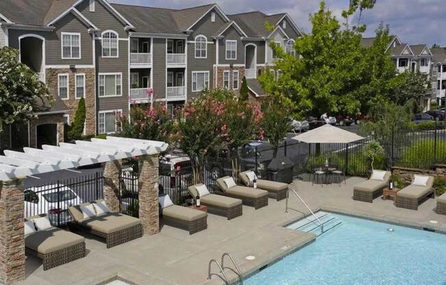 an outdoor pool with chairs and umbrellas in front of an apartment building