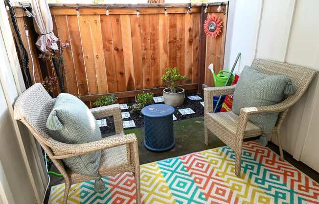 a patio with two chairs and a coffee table with a colorful rug on the ground